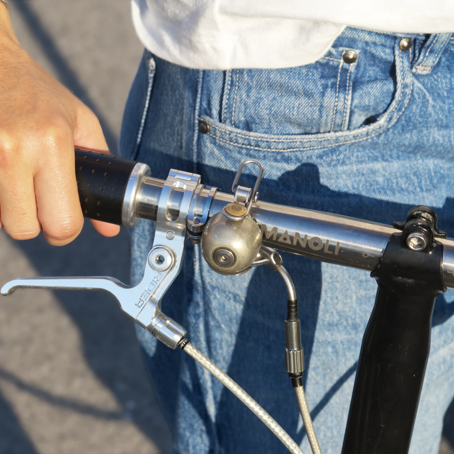 Manoli Titanlenker für Brompton mit poliertem Finish und lasergraviertem Logo – kombiniert mit hochwertigen Ledergriffen und minimalistischer Spur Cycle Klingel. Stilvolles Upgrade für anspruchsvolle Brompton-Fahrer.