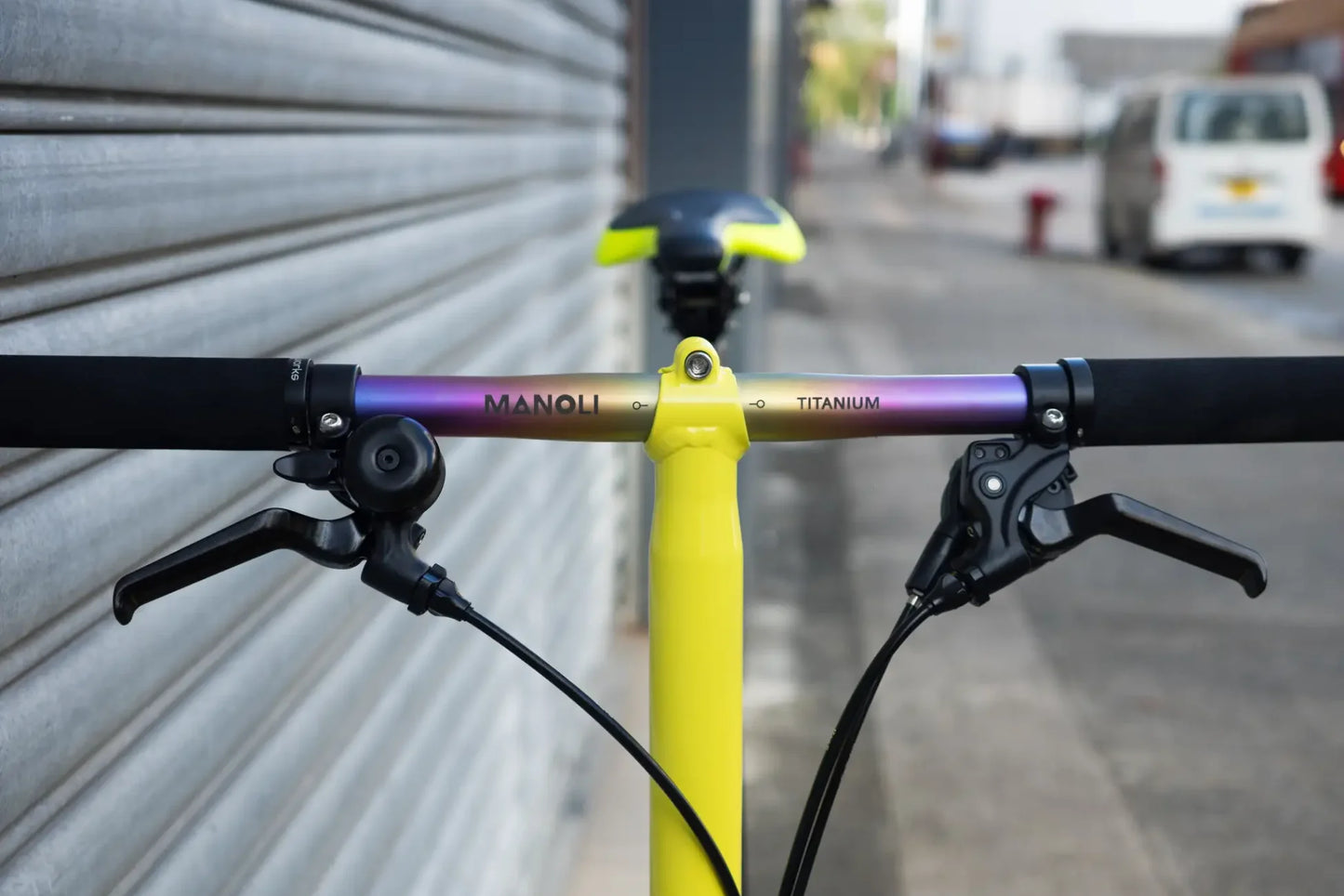Titanlenker in der auffälligen Farbe Rainbow an einem gelben Brompton Fahrrad, Ansicht von Vorne mit Fokus auf das Logo